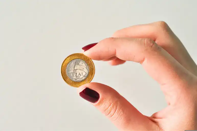 mão feminina segurando uma moeda de 1 real